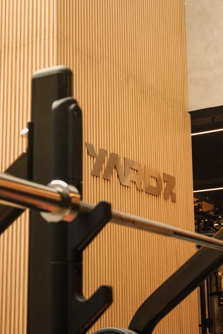 Parede ripada de madeira com o logo da YARDZ e rack de halteres