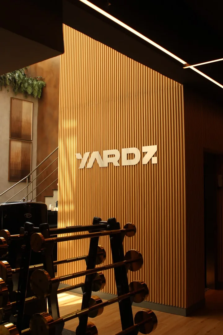 Logo da YARDZ em relevo na parede ripada, visto por trás da barra