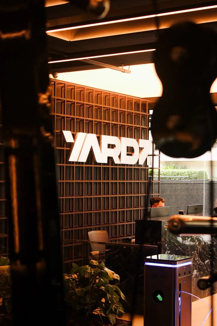 Recepção da YARDZ com o logo na parede vazada e a catraca de entrada