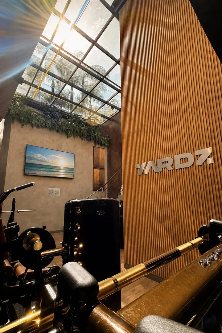 Parede ripada de madeira com o logo da YARDZ, sob o teto de vidro com a luz do sol atravessando